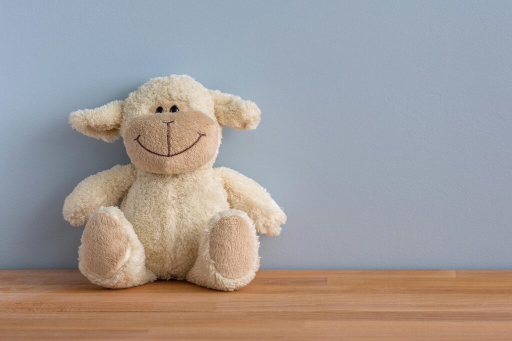 pexels-photo-12211-12211 A cuddly plush sheep toy with a big smile sits on a wooden surface against a light blue wall.